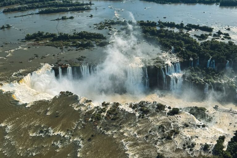 Aerial view of Iguazu Falls showing the waterfalls, river channels, rainforest and rising mist.