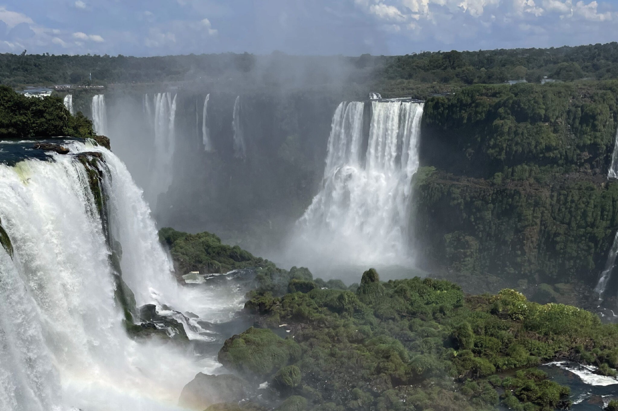 Panoramic view of Iguazu Falls surrounded by rainforest and rising mist on the Argentine side.